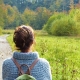 Mujer de espaldas mirando apaciblemente un campo verde y arbolado