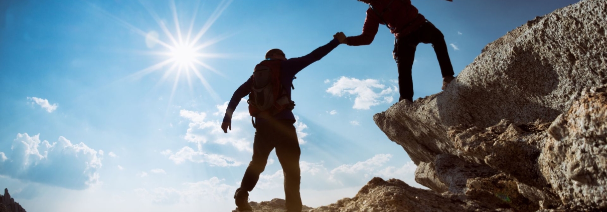 Dos personas en una montaña, donde una ayuda a la otra a subir, simbolizando confianza, colaboración y el poder de la comunicación efectiva para construir relaciones sólidas y de alto impacto.